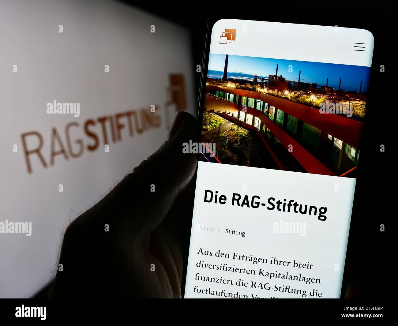 Person holding cellphone with website of German foundation RAG-Stiftung in front of logo. Focus on center of phone display. Stock Photo