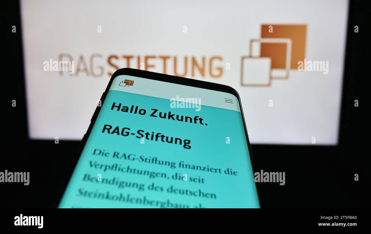 Smartphone with webpage of German foundation RAG-Stiftung in front of logo. Focus on top-left of phone display. Stock Photo