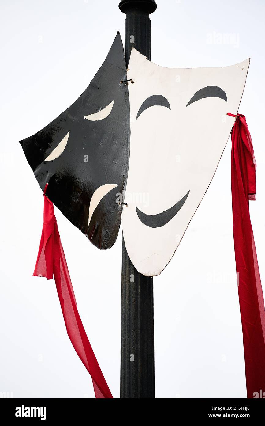 Two black and white theater masks with a red ribbon hanging on a pole Stock Photo