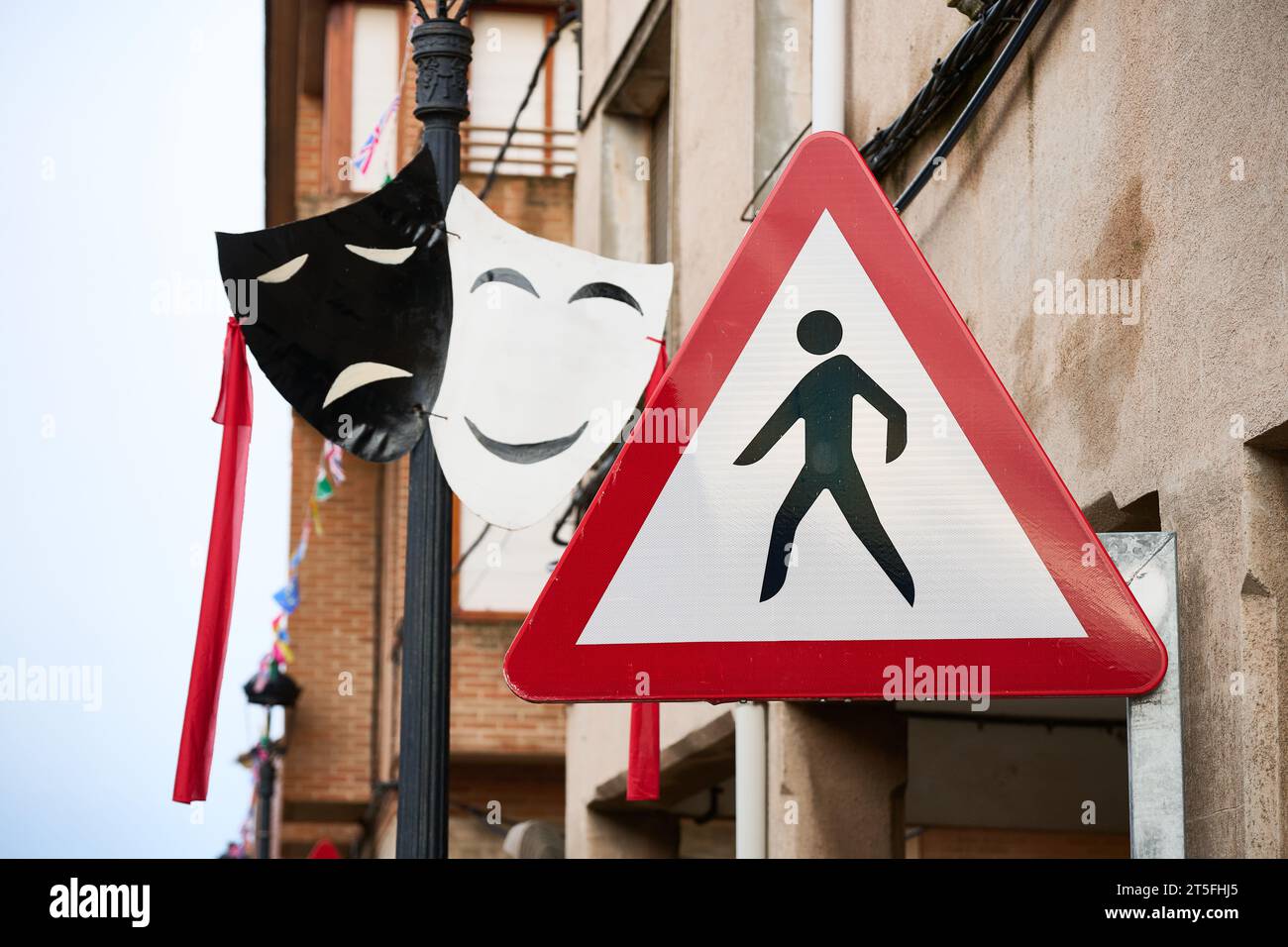 Two black and white theater masks with a red ribbon hanging on a pole with a crosswalk sign next to them Stock Photo