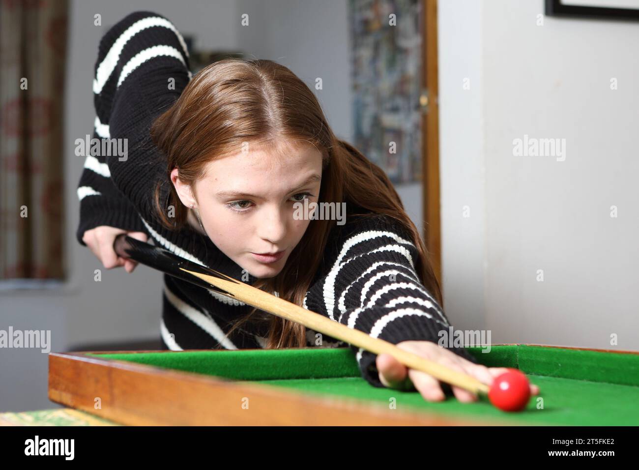 Teenage girl playing traditional pub game of bagatelle in lounge at home Stock Photo