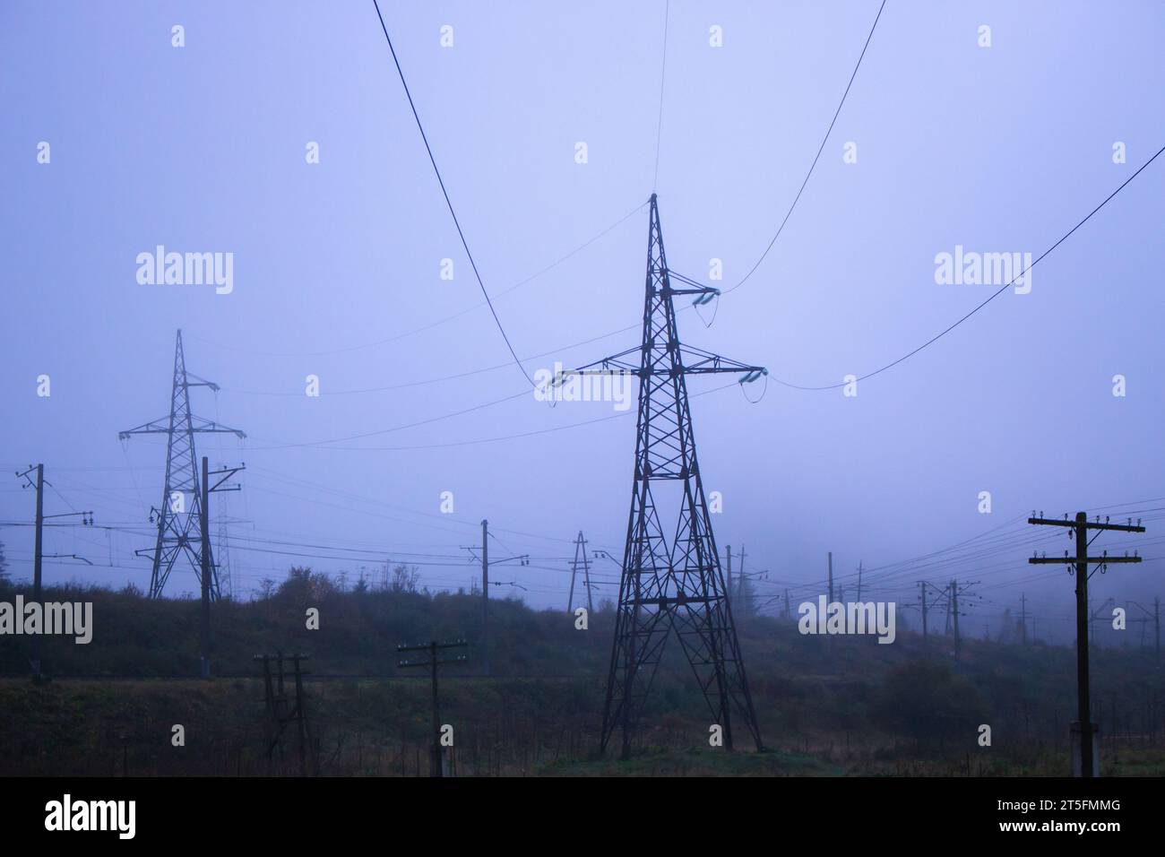 Power lines in foggy morning in autumn field. Electrical industry concept. Electricity equipment in nature. High voltage concept. Power lines. Stock Photo