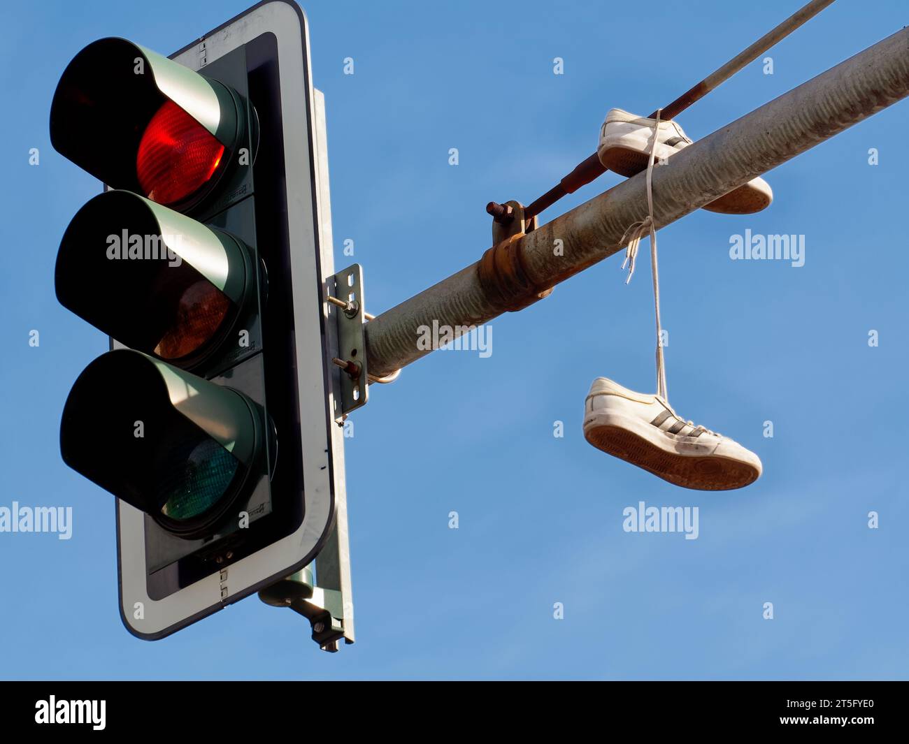 Traffic lights showing red and a pair of Adidas shoes hanging on the traffic light pole against a blue sky at Frankfurter Tor in Berlin. Stock Photo