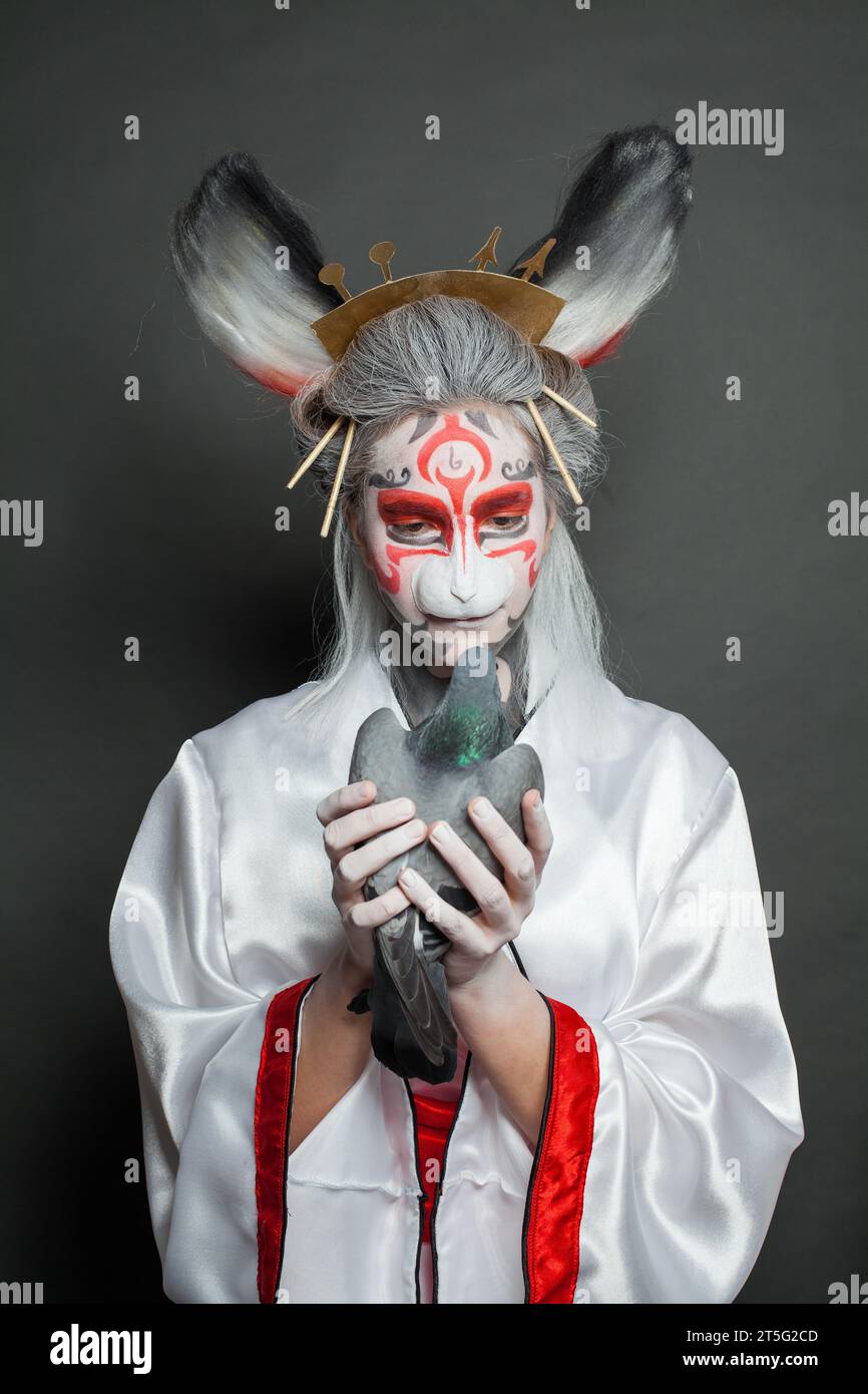 Fashion portrait of young actress woman with animal makeup, mask and stage asian costume standing on black background. Halloween, carnival, performanc Stock Photo