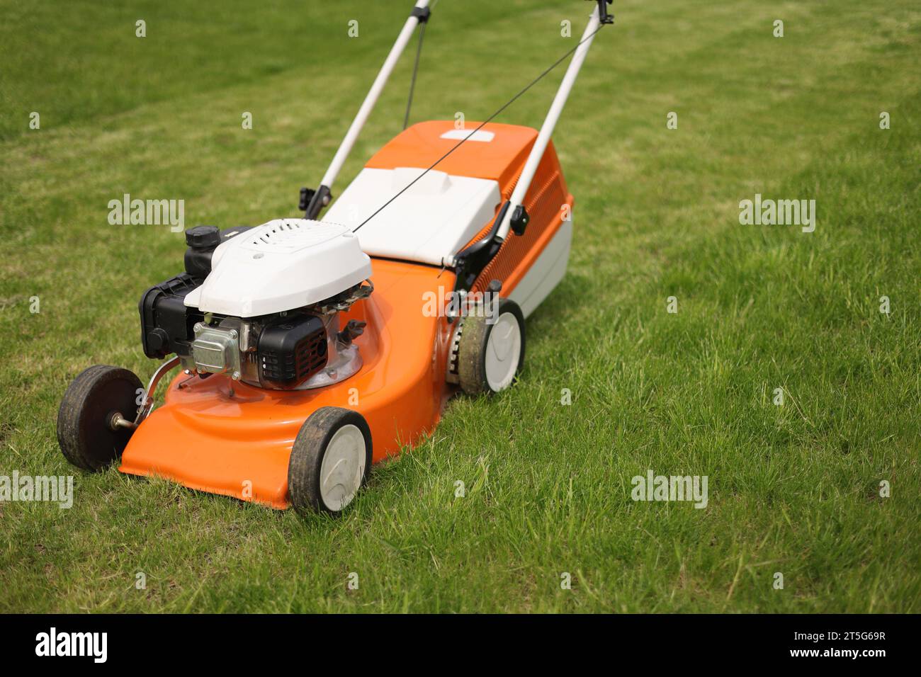 Top view of modern orangegrey electric lawn mower cutting bright lush