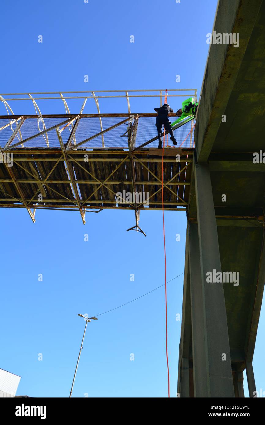Young people practicing abseiling on a wooden and metal bridge with a blue sky in the background. bottom view. selective focus Stock Photo