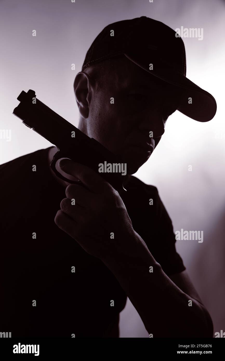 Young criminal killer in cap with gun pistol in dark silhouette photo book cover thriller design. Stock Photo