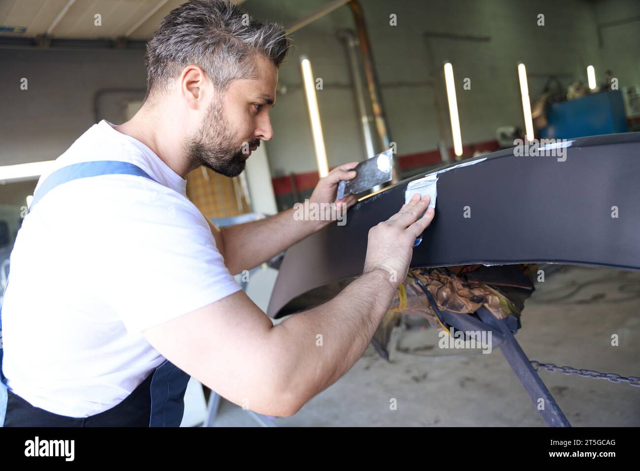 Focused car mechanic removing scratches from auto body part Stock Photo