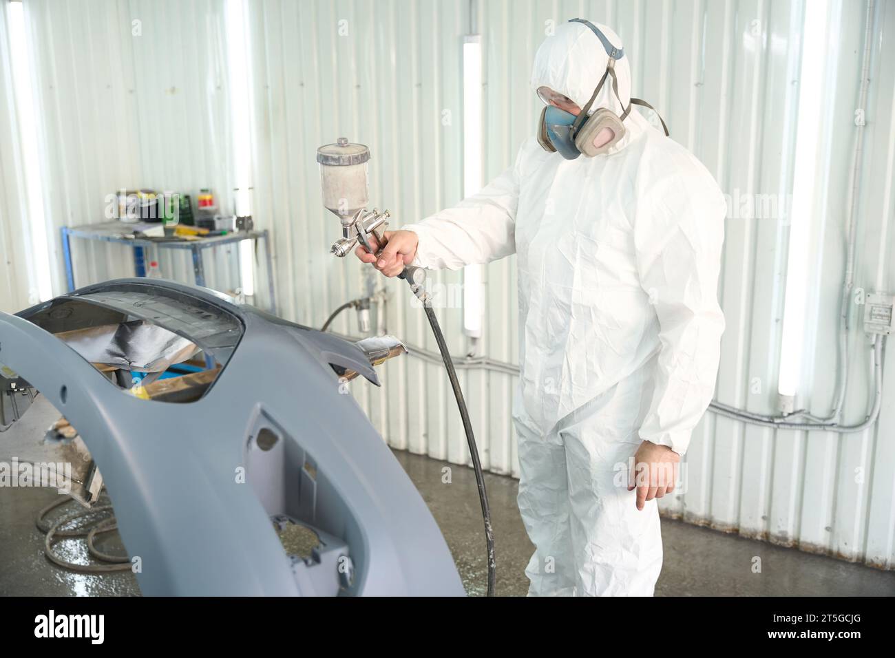 Car detailing worker spray-painting auto body panel in repair shop Stock Photo