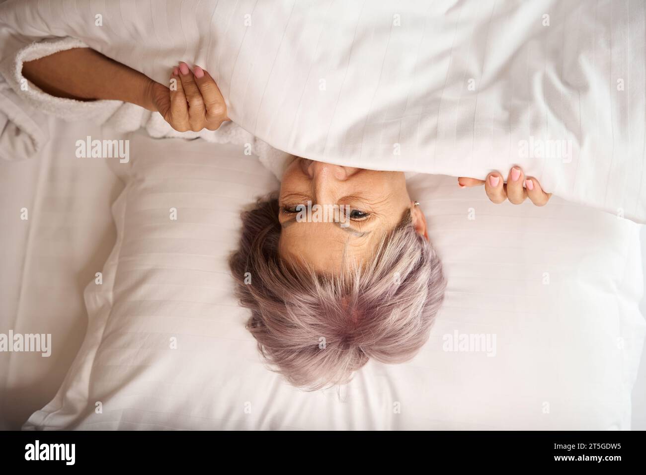 Joyful elderly woman looks out from under the blanket Stock Photo