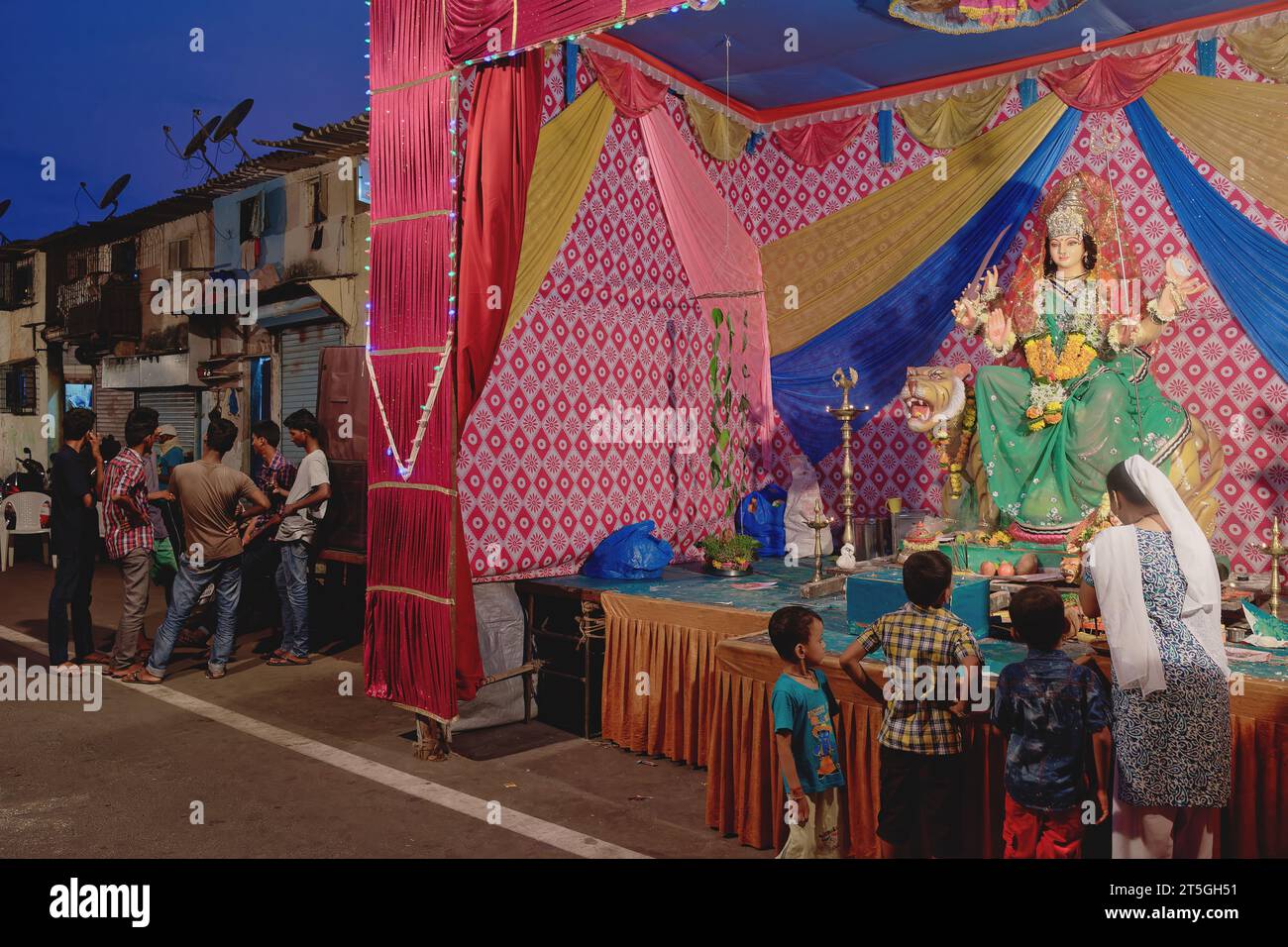During Hindu festival Durga Puja, a woman and her children visit a shrine with a figure of goddess Durga; in a slum area in Walkeshwar, Mumbai, India Stock Photo