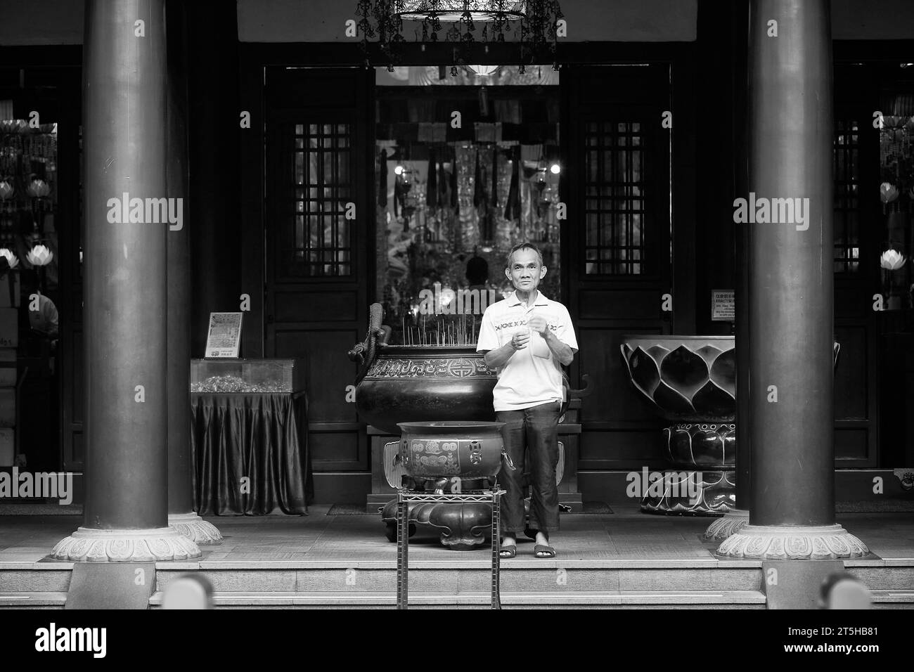 Black And White Photo Of An Asian Man Holding Incense, Standing At The Entrance To The Buddha Tooth Relic Temple, Singapore. Stock Photo