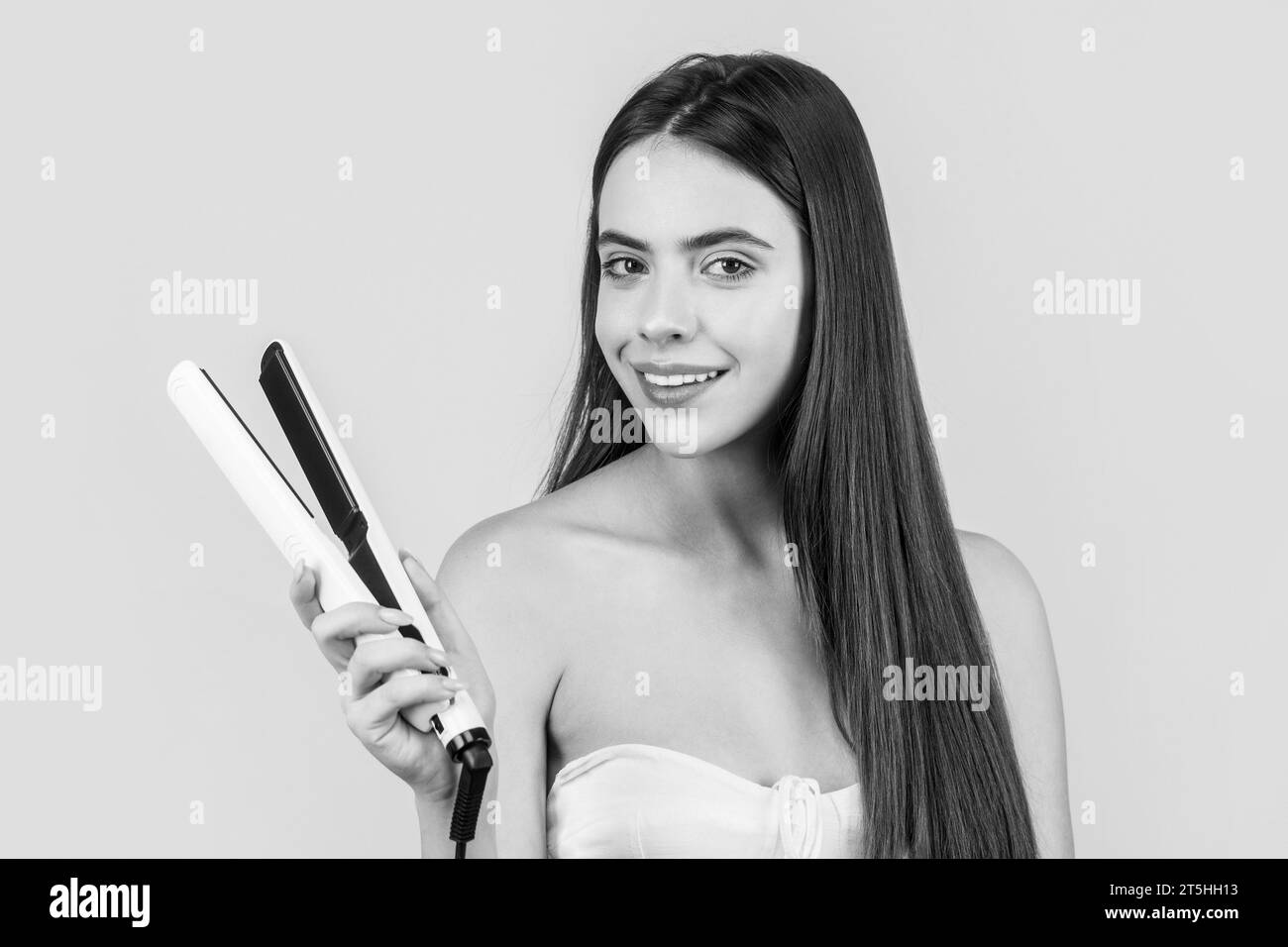 Hairstyle. Beautiful smiling woman ironing long hair with flat iron. Black and white Stock Photo
