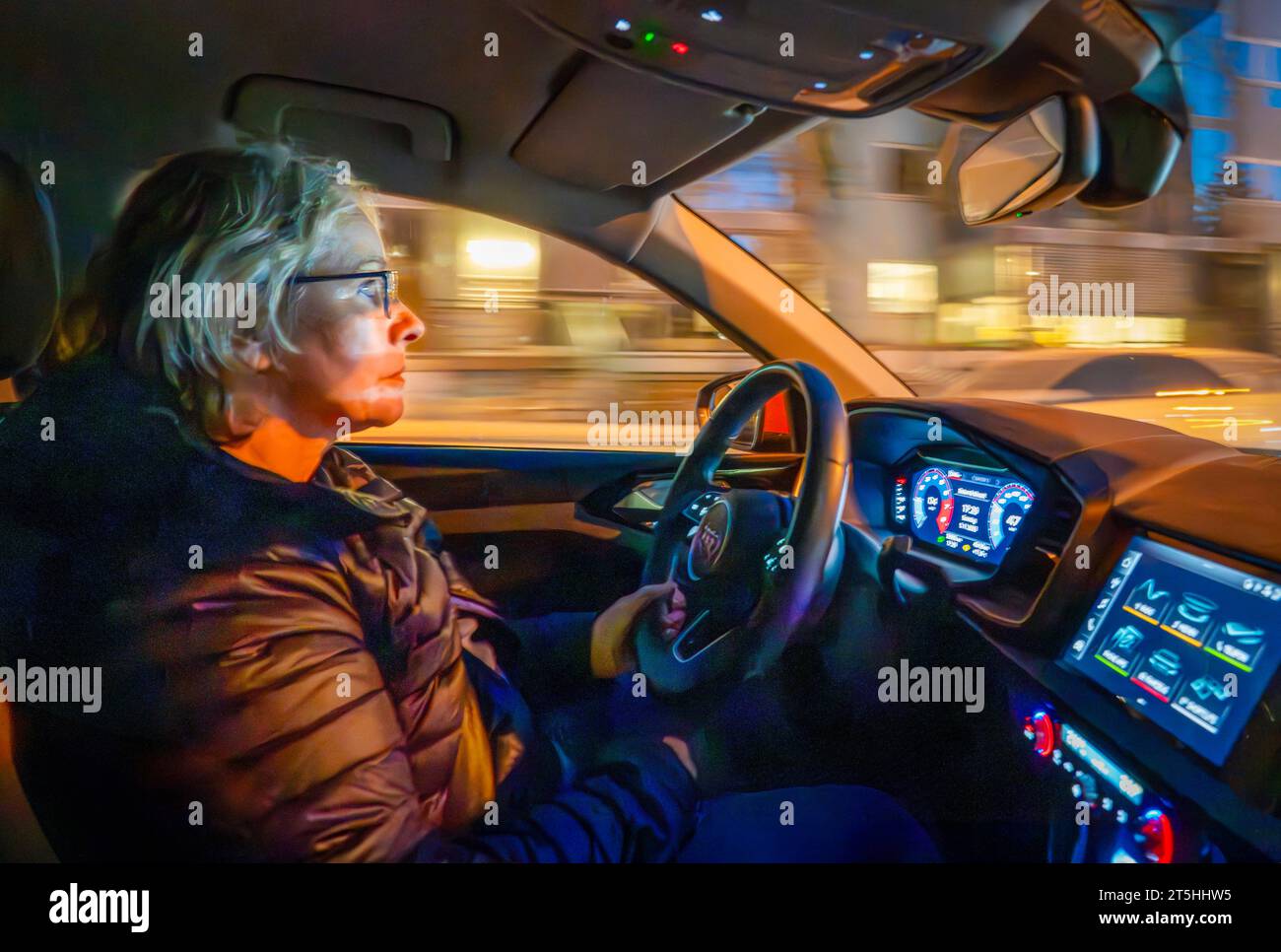 ältere Autofahrerin fährt abends im Dunkeln in der Stadt, München, November 2023 Deutschland, München, November 2023, ältere Autofahrerin, Ü60, am Steuer, fährt abends im Dunkeln durch die Stadt, Frau ist geblendet von entgegenkommenden Fahrzeugen, Symbolfoto, Brille tragen beim Autofahren, Sehstärke, Augenprobleme, Sehschwierigkeiten, Sicht, Blendung, Fahren bei Dunkelheit, Stress, Senioren, Seniorin, Unfallgefahr, Licht, Babyboomer, Herbst, Winter, *** elderly female driver driving in the evening in the dark in the city, Munich, November 2023 Germany, Munich, November 2023, elderly female dr Stock Photo