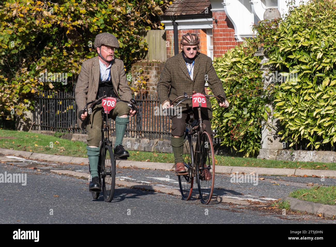 5th November 2023. Participants in the London to Brighton Veteran Car Run 2023 driving through West Sussex, England, UK. The route of the popular annual event runs for 60 miles. Pictured: Two men riding old bicycles wearing retro tweed clothes, one with a leather bicycle helmet. On the left (number 708) an 1895 Crypto cycle standard model body and on the right (no 705) an 1891 New Mail safety bicycle. Stock Photo