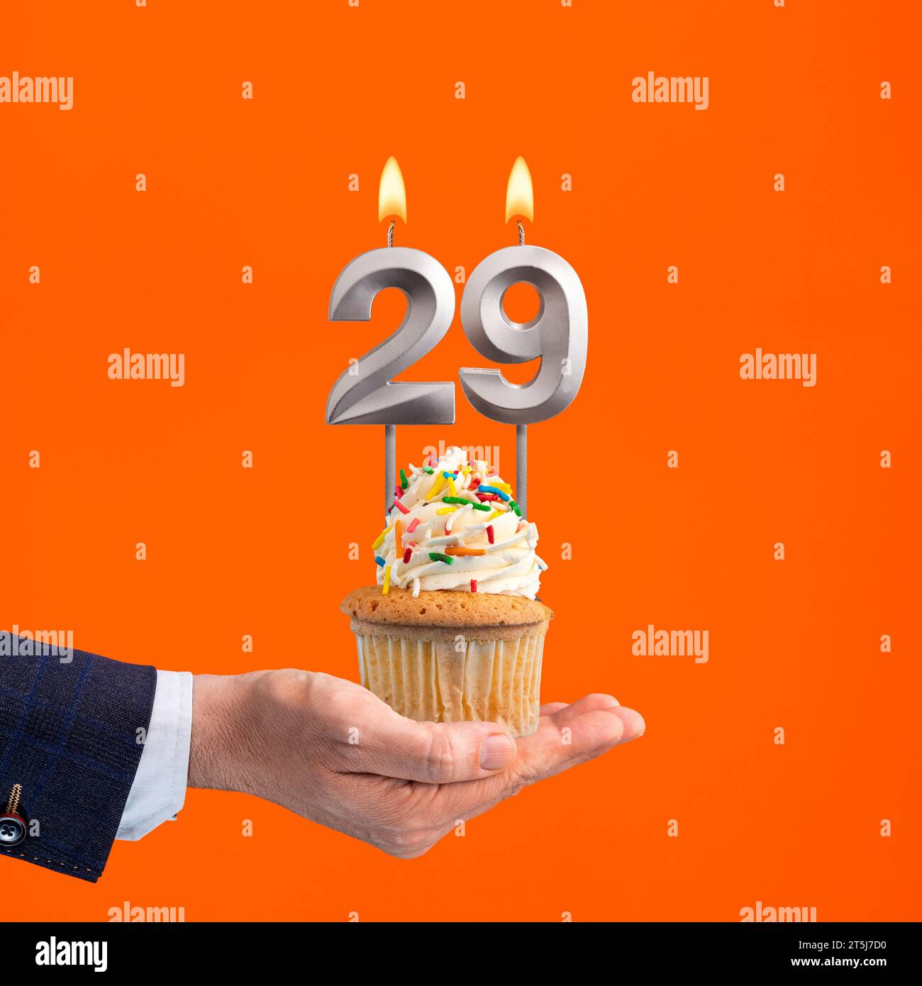The hand that delivers cupcake with the number 29 candle - Birthday on orange background Stock Photo