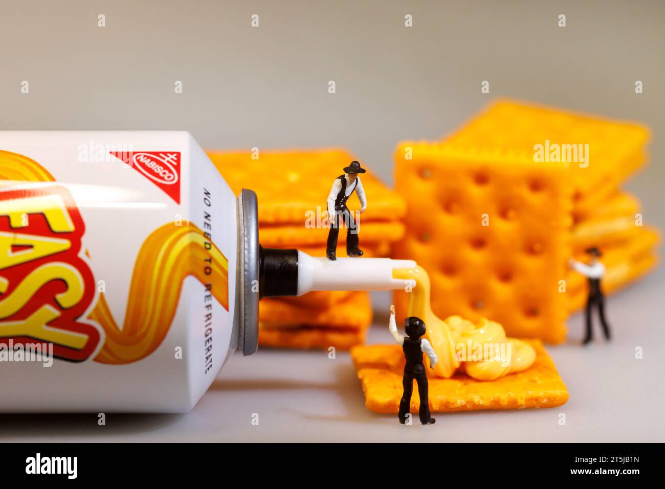 Miniature People Working on Life Size Cheese and Crackers Stock Photo