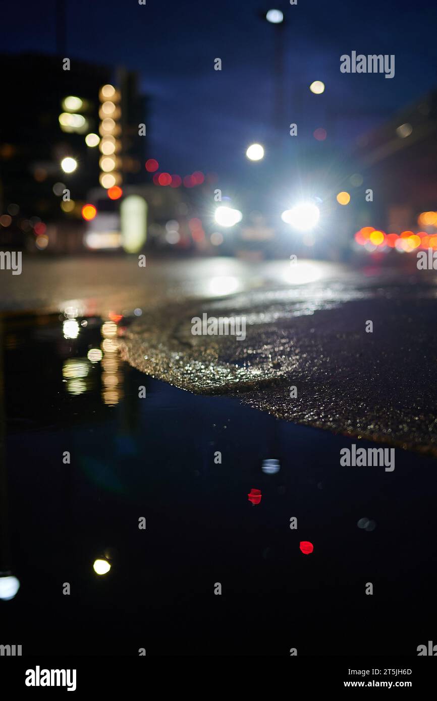 Out of focus view of cars passing at street level at night with reflection in puddle Stock Photo