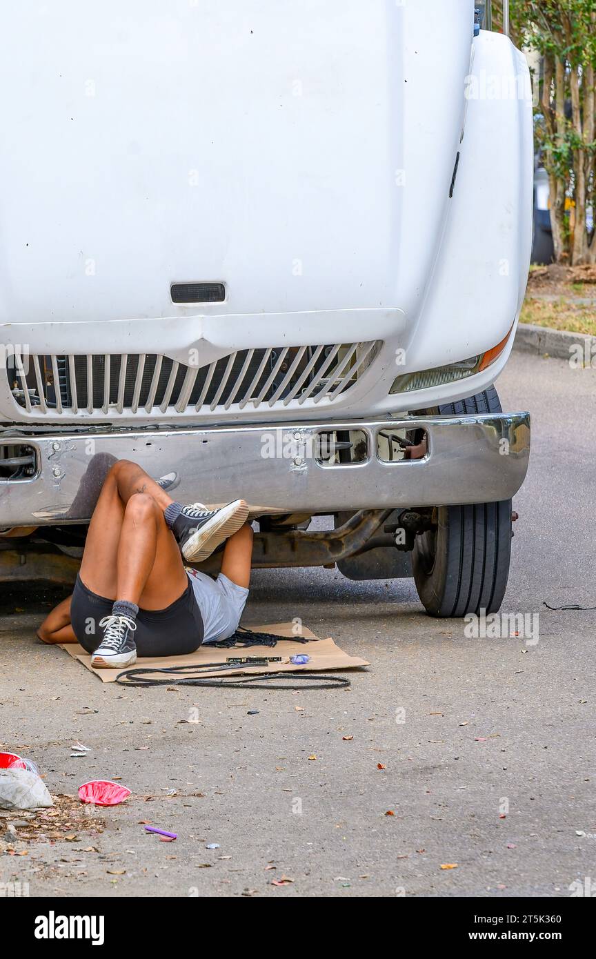 NEW ORLEANS, LA, USA - OCTOBER 29, 2023: Woman laying on her back under the front of a large truck replacing the fan belt. Stock Photo