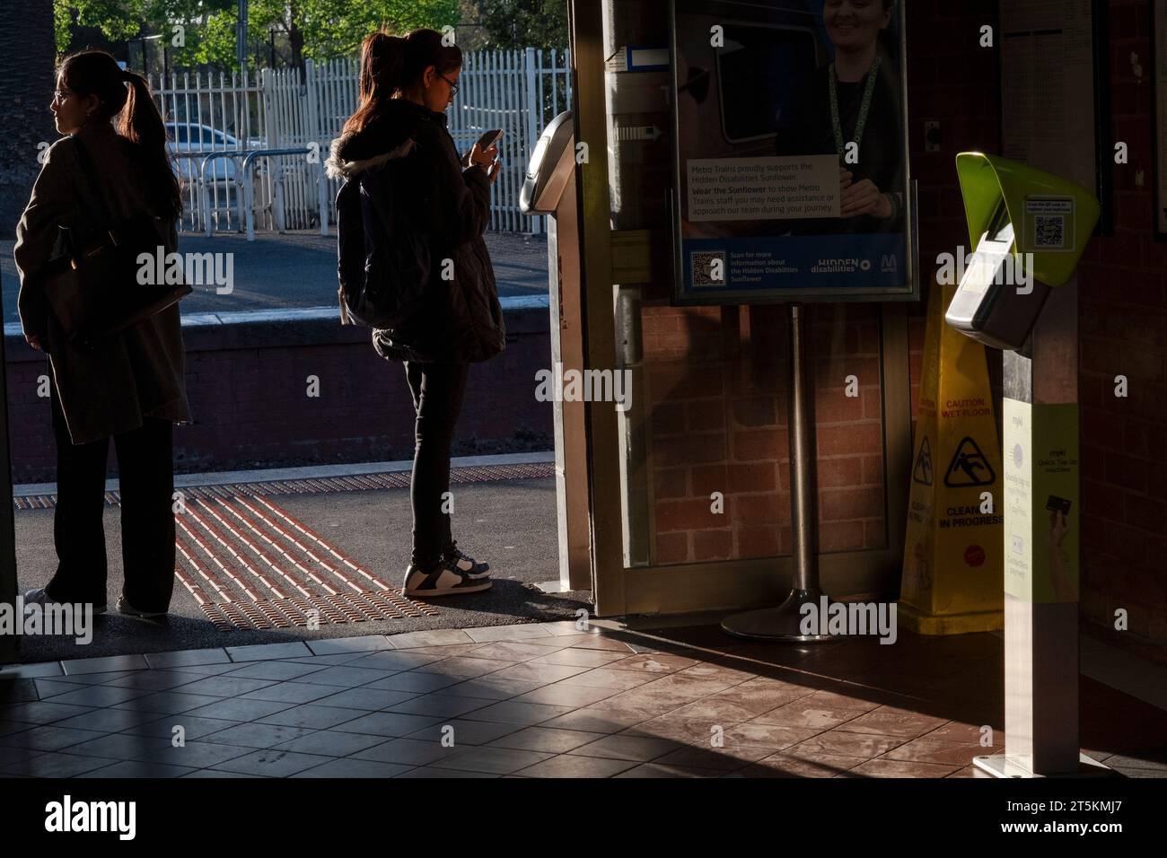 Passengers check their tickets on a mobile phone at a vendor machine on the platform of a suburban railway station. Clifton Hill, Victoria, Australia Stock Photo