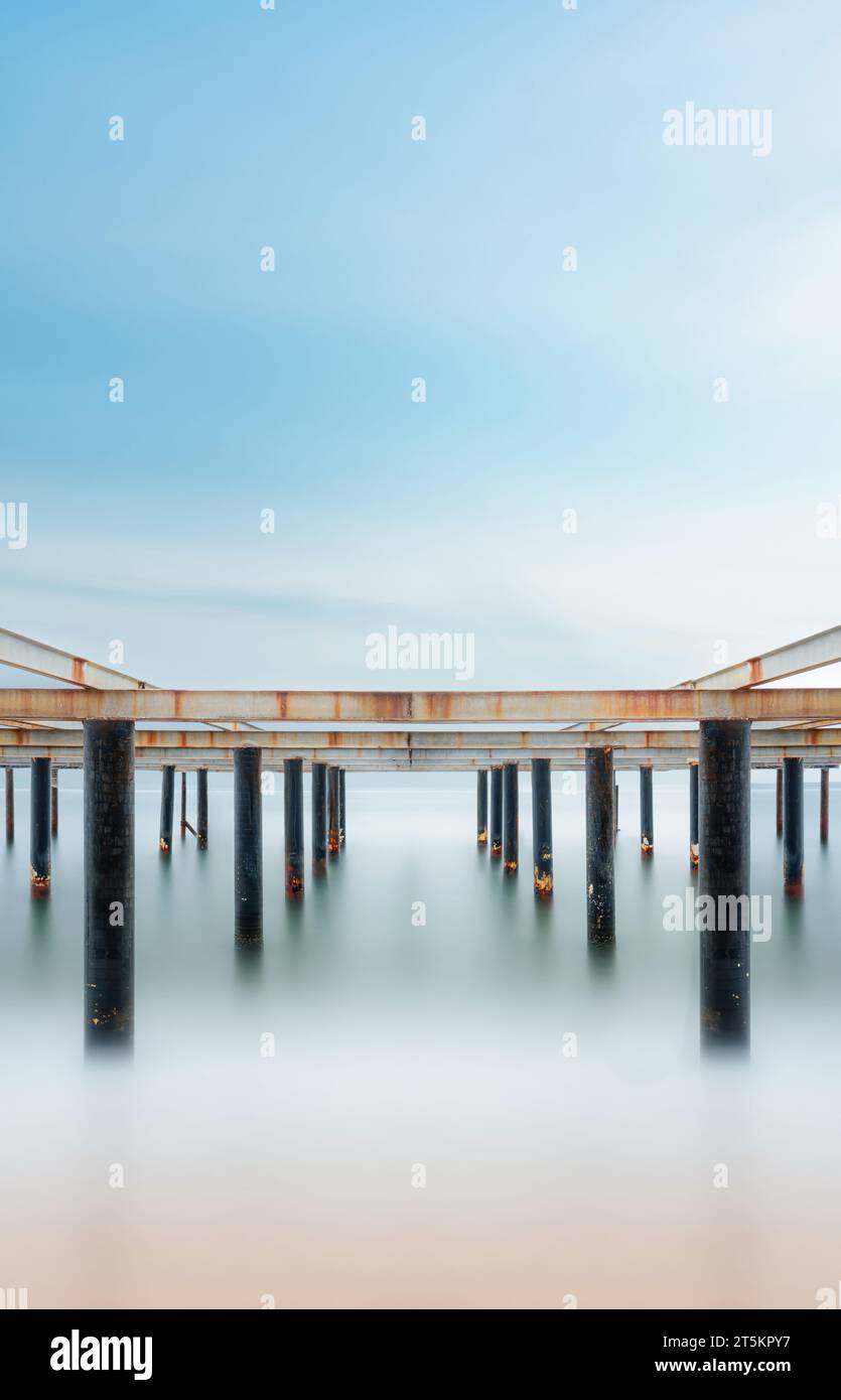 Fine art view of columns under metal pier at sunrise. Shot with long exposure to make the sea appear as fog Stock Photo