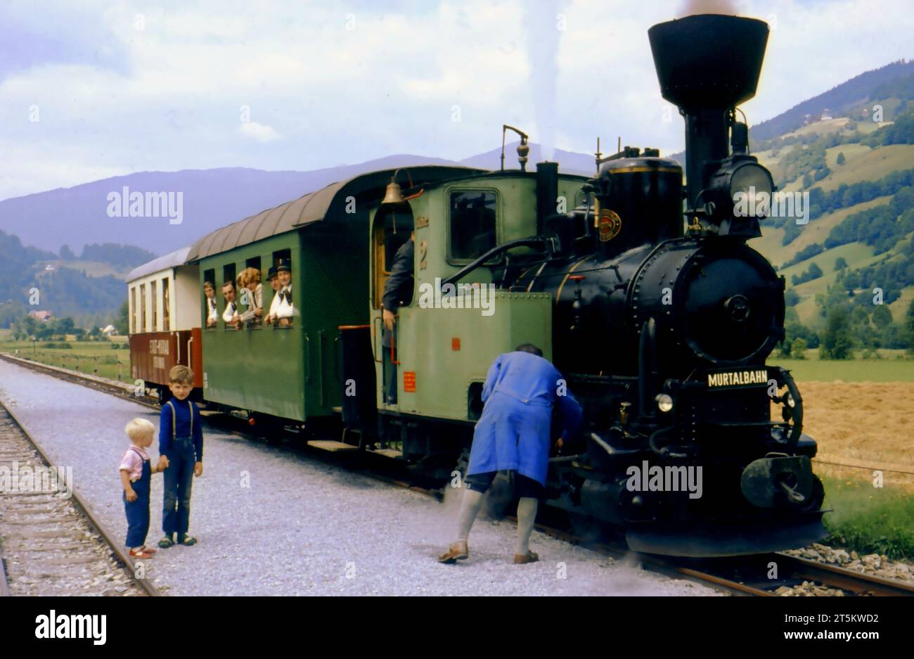 A Murtalbahn train with two wagons in St. Lorenzen, Styria, Austria. People are looking out of the windows. Approx. 1972. Editorial use only. Stock Photo