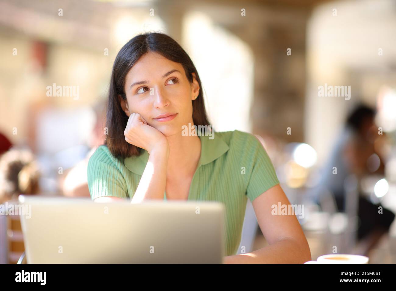 Front view portrait of a serious woman with laptop thinking looking at side in a bar terrace Stock Photo