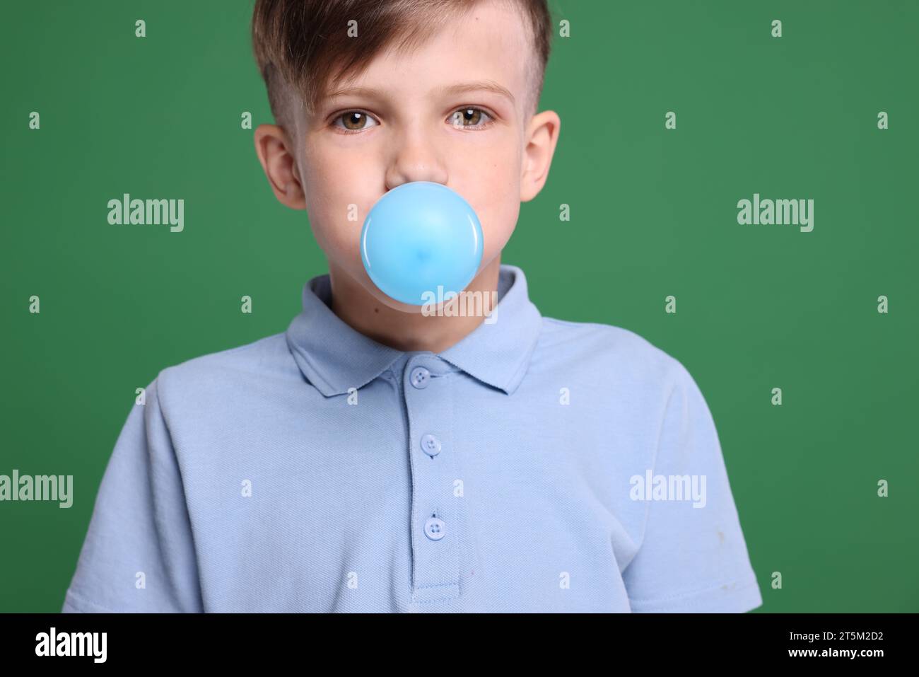 Boy blowing bubble gum on green background Stock Photo