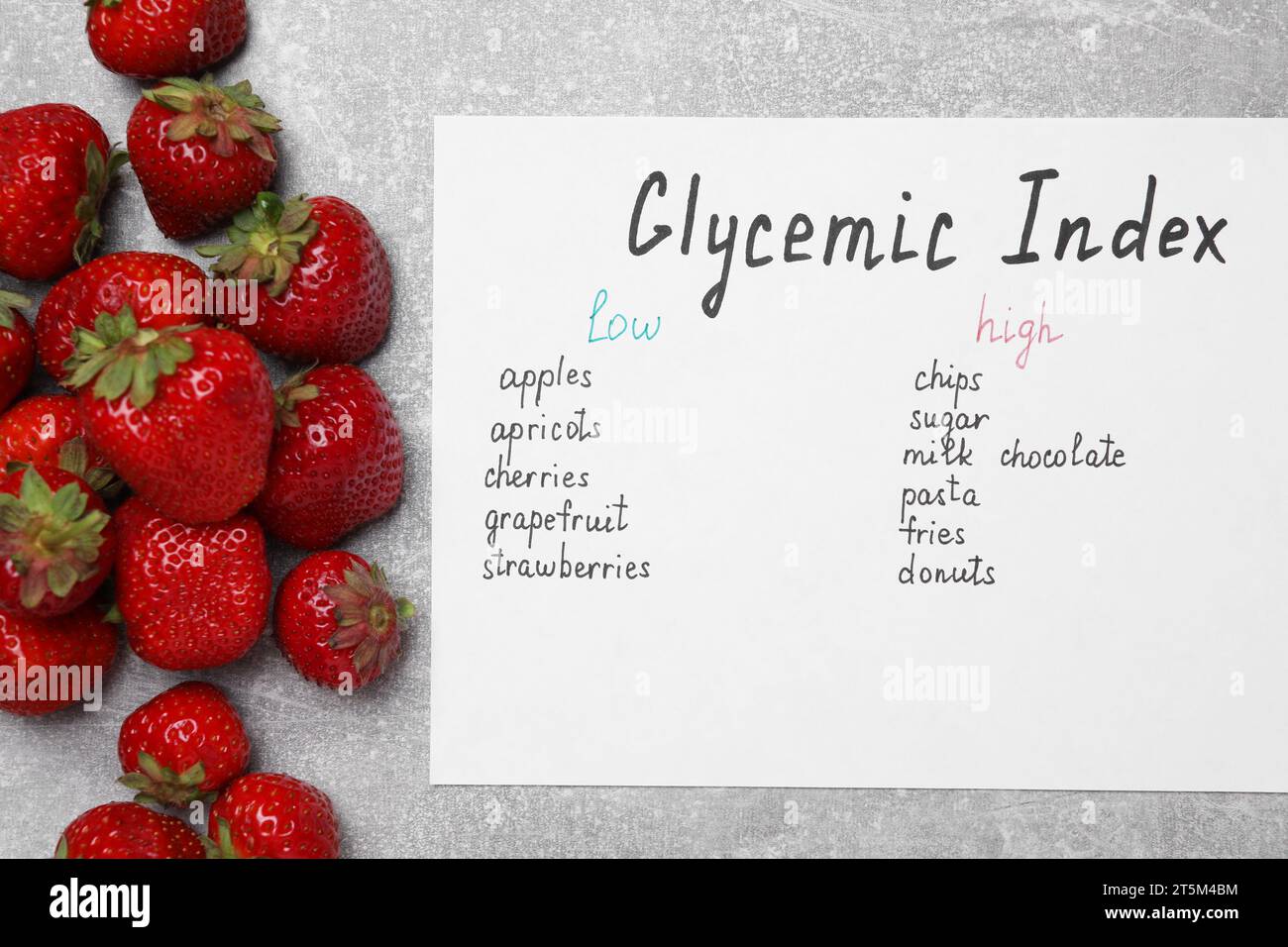 List with products of low and high glycemic index and strawberries on light grey table, top view Stock Photo