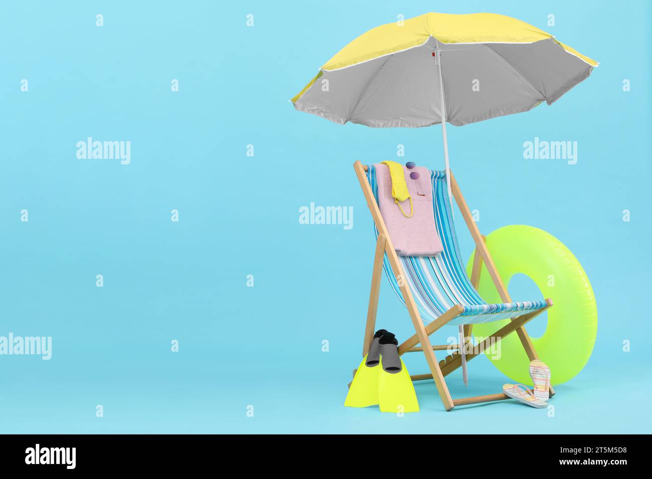 Deck chair, umbrella and beach accessories against light blue ...