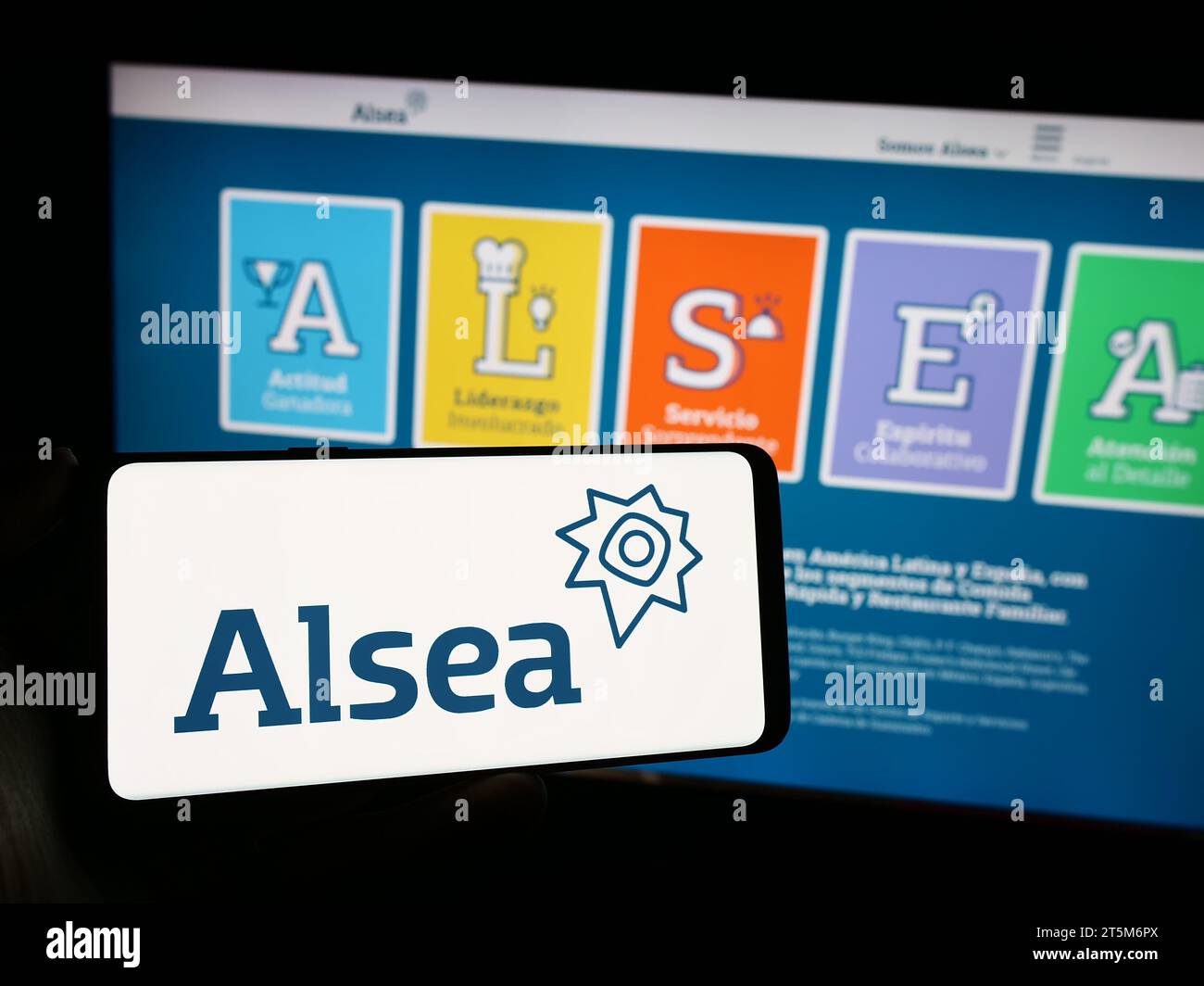 Person holding cellphone with logo of Mexican restaurant company Alsea S.A.B. de C.V. in front of business webpage. Focus on phone display. Stock Photo