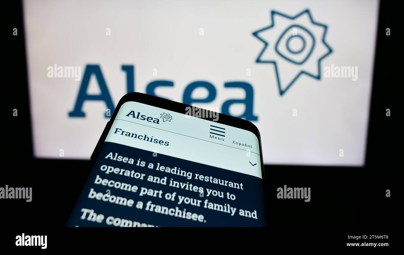 Smartphone with website of Mexican restaurant company Alsea S.A.B. de C.V. in front of business logo. Focus on top-left of phone display. Stock Photo