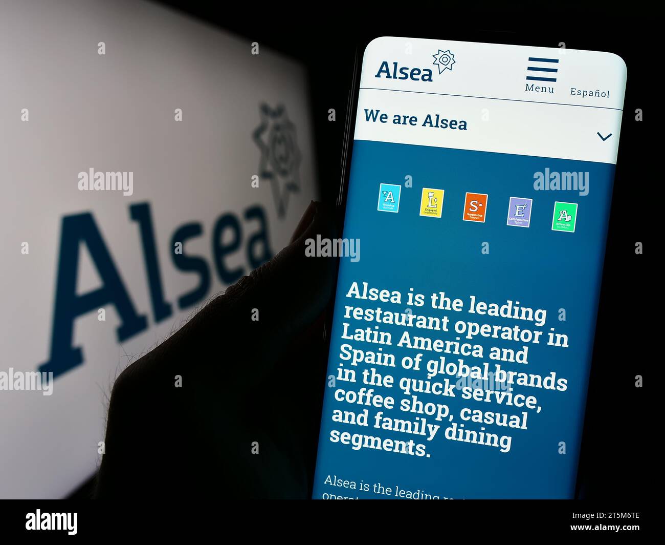 Person holding cellphone with webpage of Mexican restaurant company Alsea SAB de CV in front of logo. Focus on center of phone display. Stock Photo