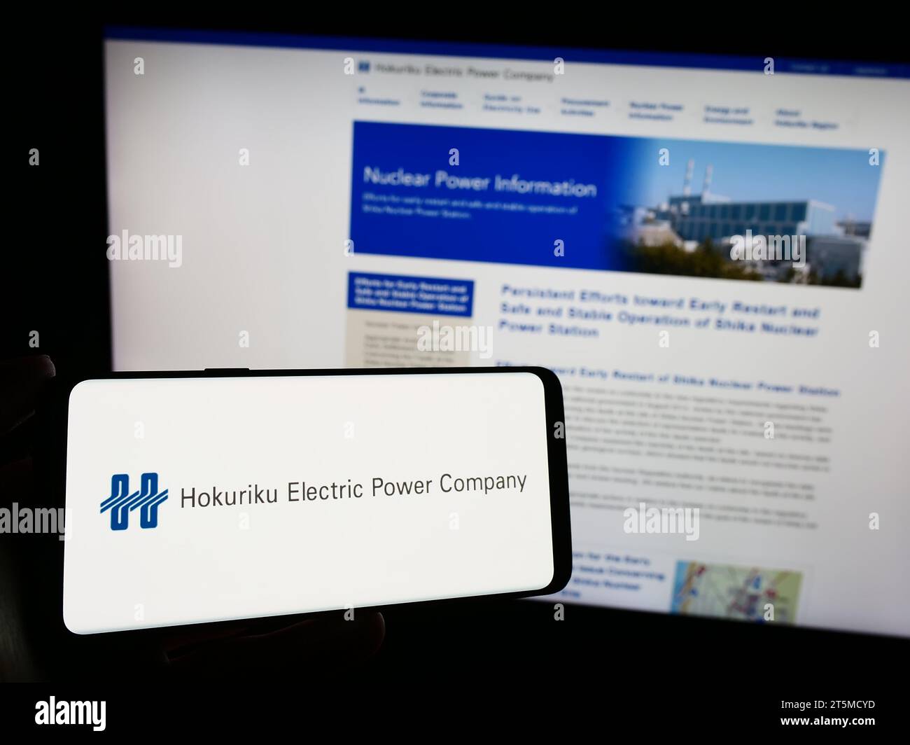 Person holding smartphone with logo of Japanese energy business Hokuriku Electric Power Company in front of website. Focus on phone display. Stock Photo