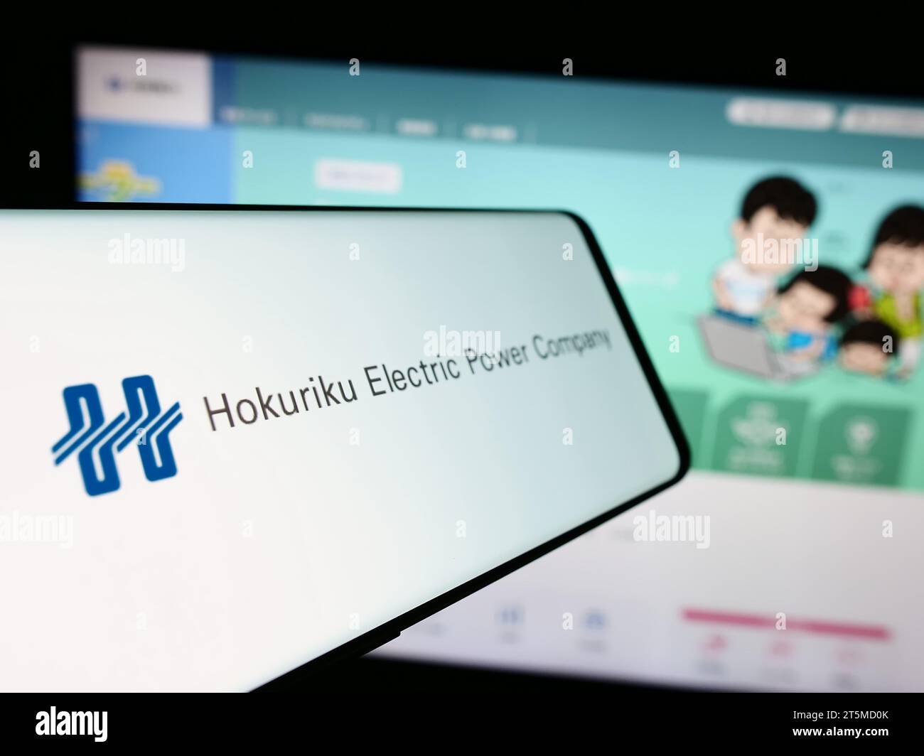 Cellphone with logo of Japanese energy business Hokuriku Electric Power Company in front of website. Focus on center-left of phone display. Stock Photo