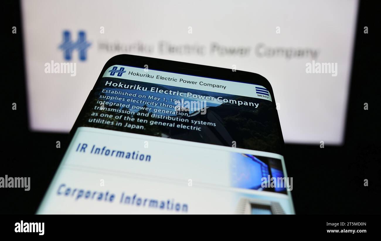 Mobile phone with website of Japanese energy business Hokuriku Electric Power Company in front of logo. Focus on top-left of phone display. Stock Photo