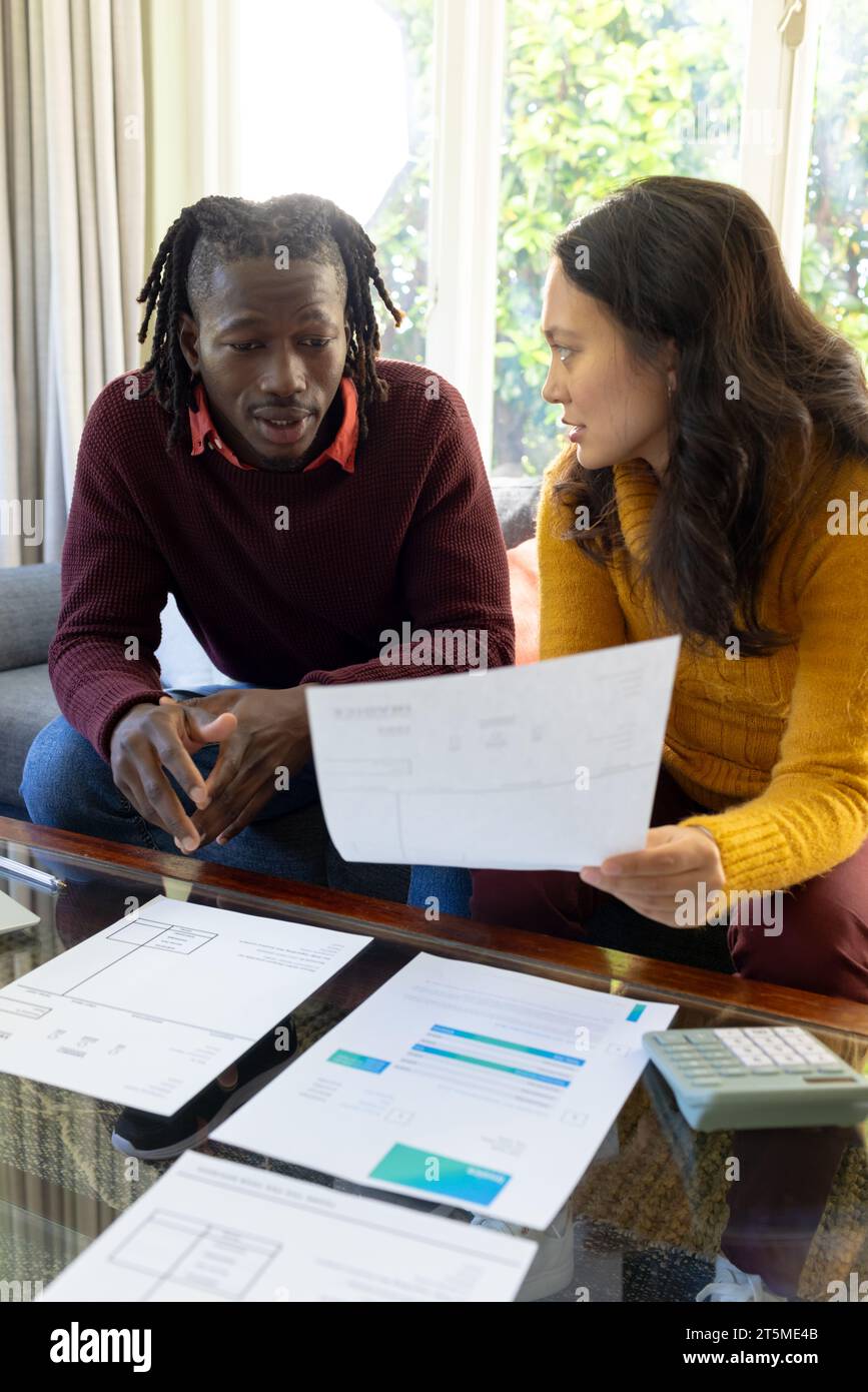 Serious diverse couple sitting on couch discussing bills and domestic finances in living room Stock Photo