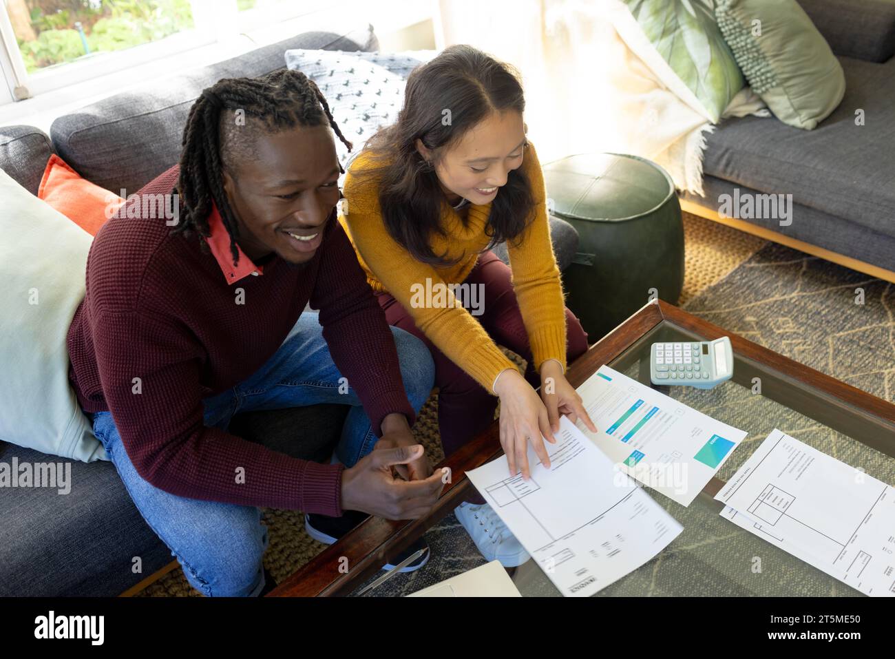 Happy diverse couple sitting on couch discussing bills and domestic finances in living room Stock Photo