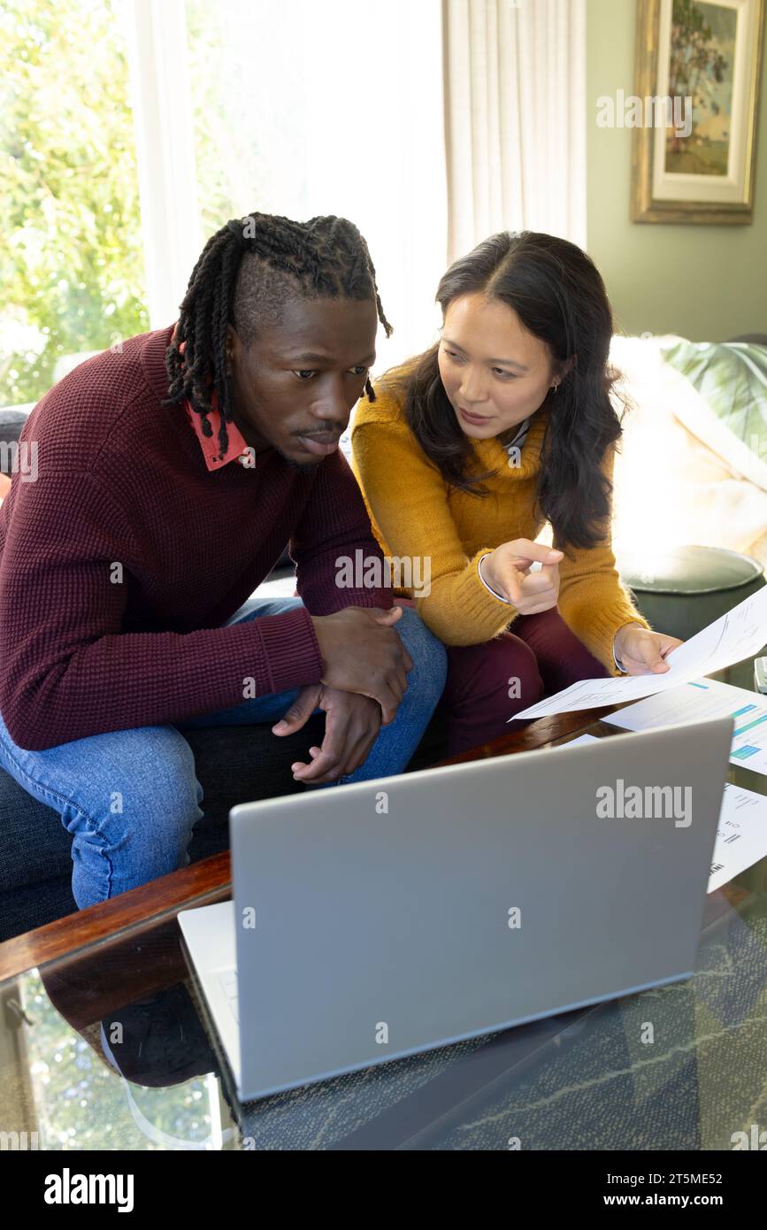 Serious diverse couple sitting on couch using laptop discussing bills and finances in living room Stock Photo