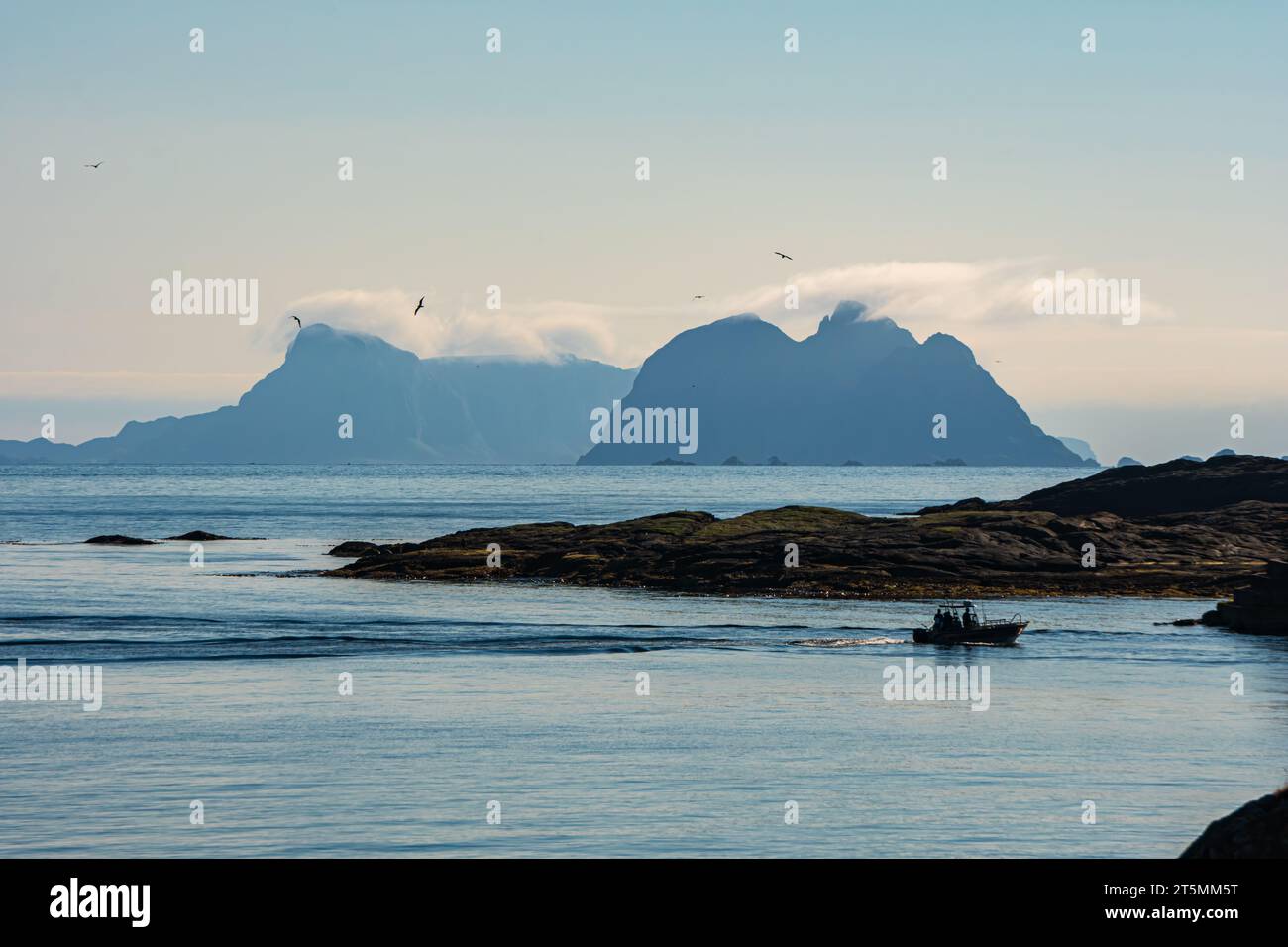 Distant mountains in Lofoten, hazy sky, boat, calm sea. Værøy in the distance. Stock Photo