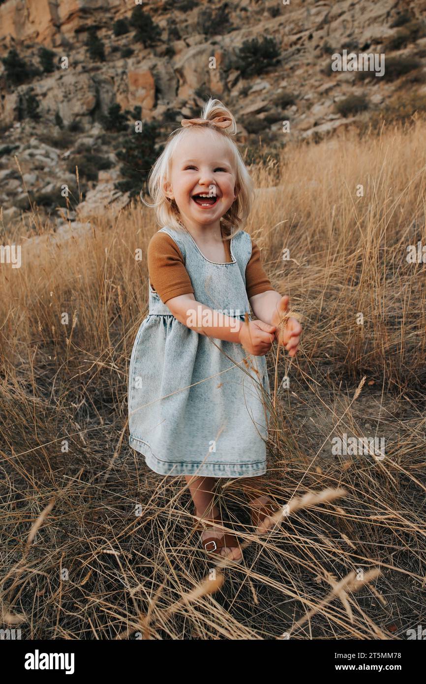 2-year-old girl stands outside, laughing with joy.' Stock Photo