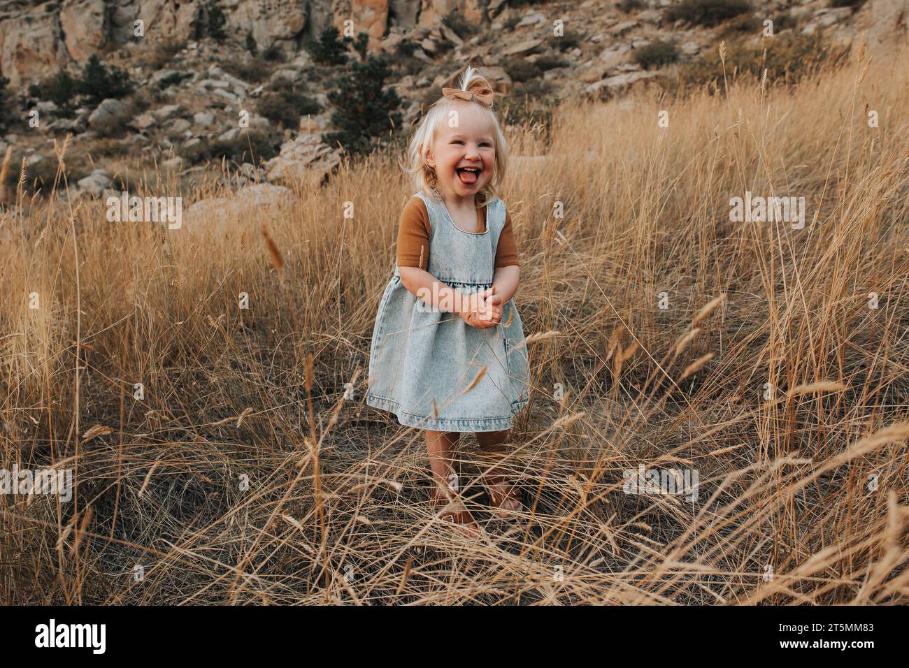 2-year-old girl stands outside, laughing with joy Stock Photo
