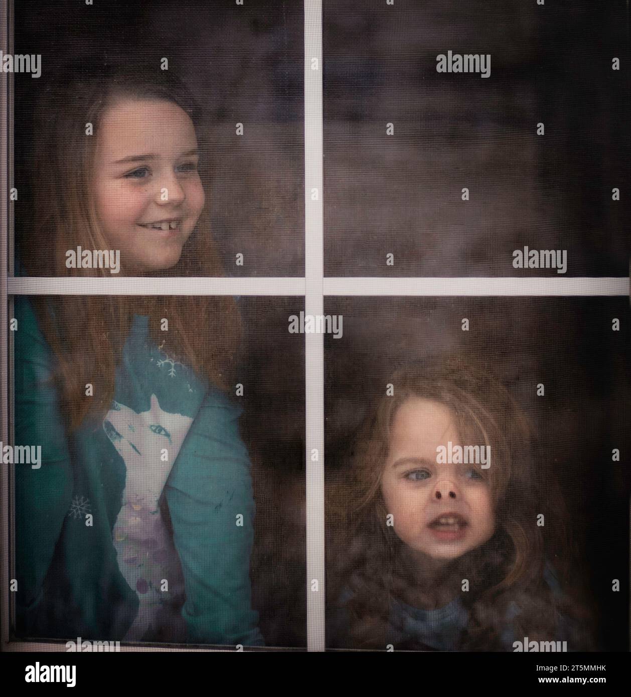 Sisters looking out window with face smashed against glass Stock Photo