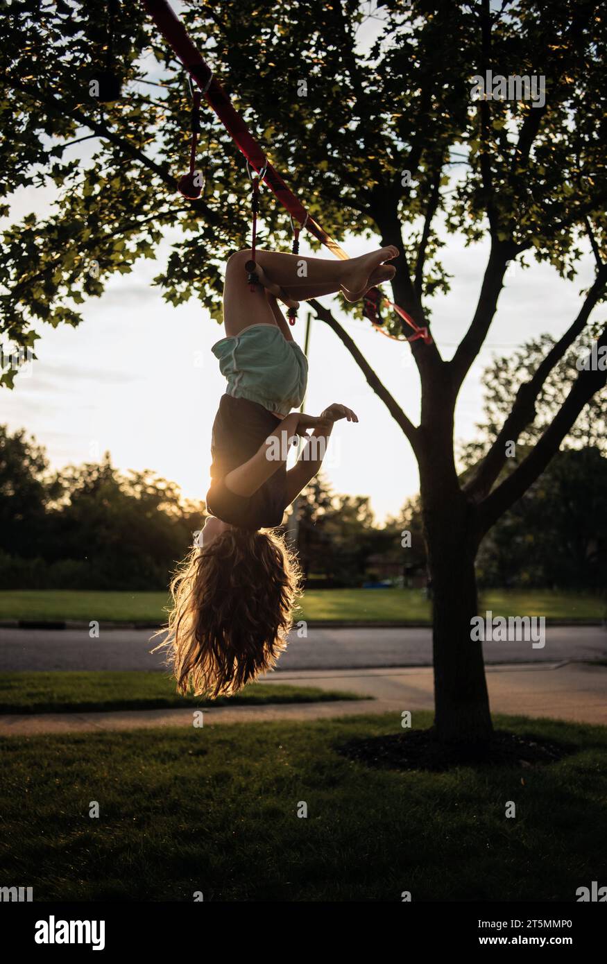 Young girl hanging upside down from tree in summer Stock Photo