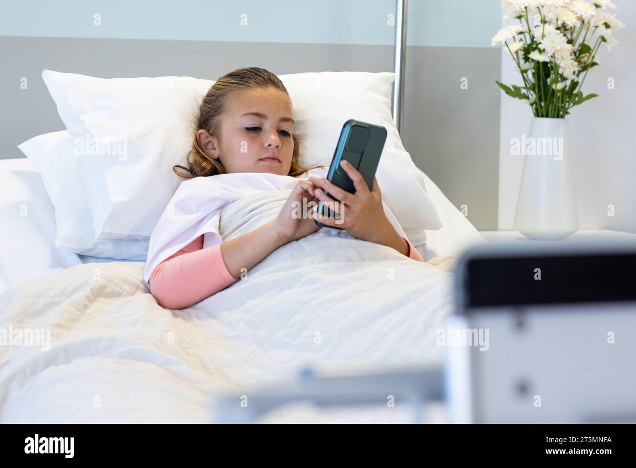 Caucasian girl patient lying in hospital bed using smartphone Stock Photo