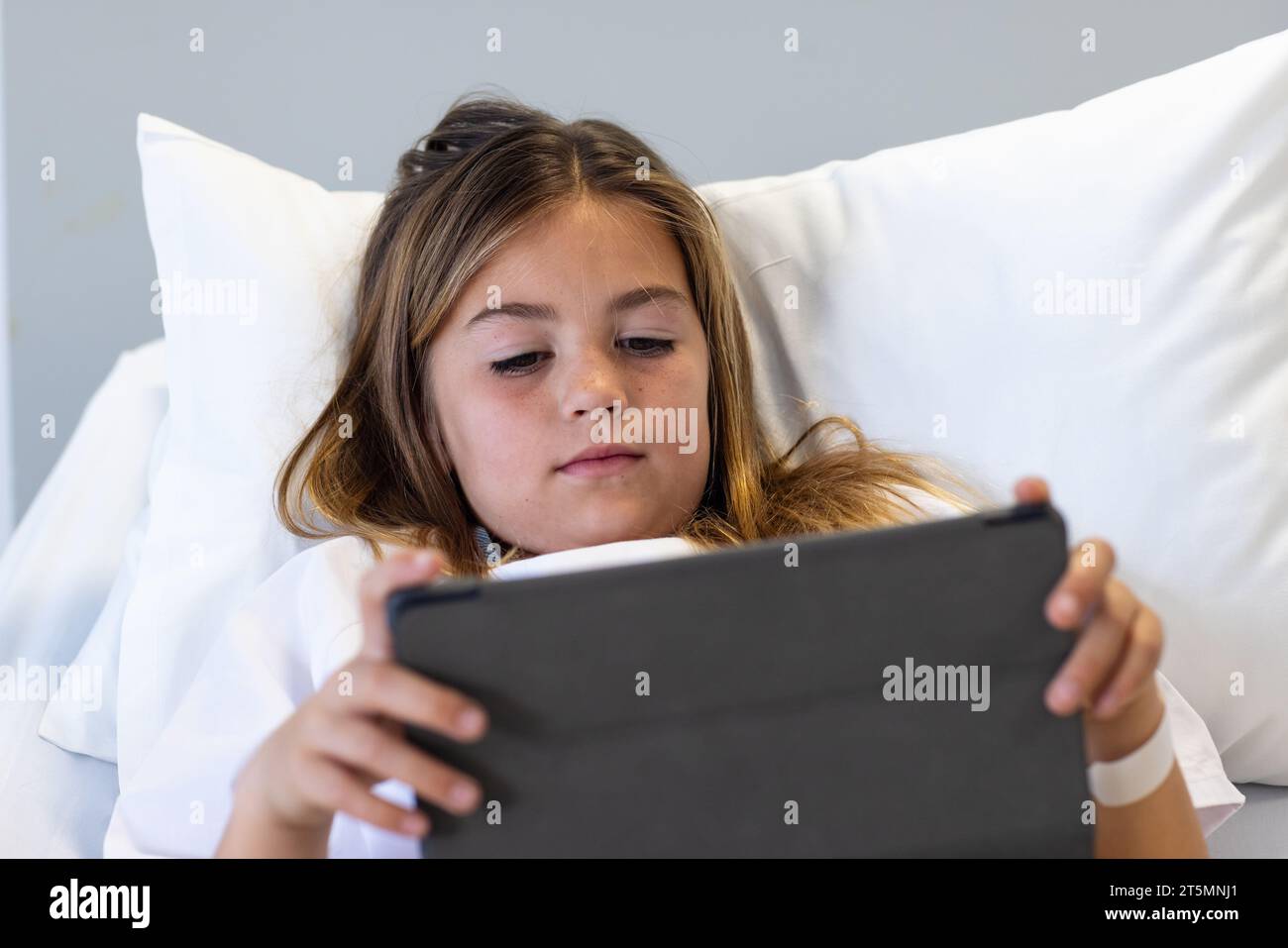 Caucasian girl patient lying in hospital bed using tablet Stock Photo
