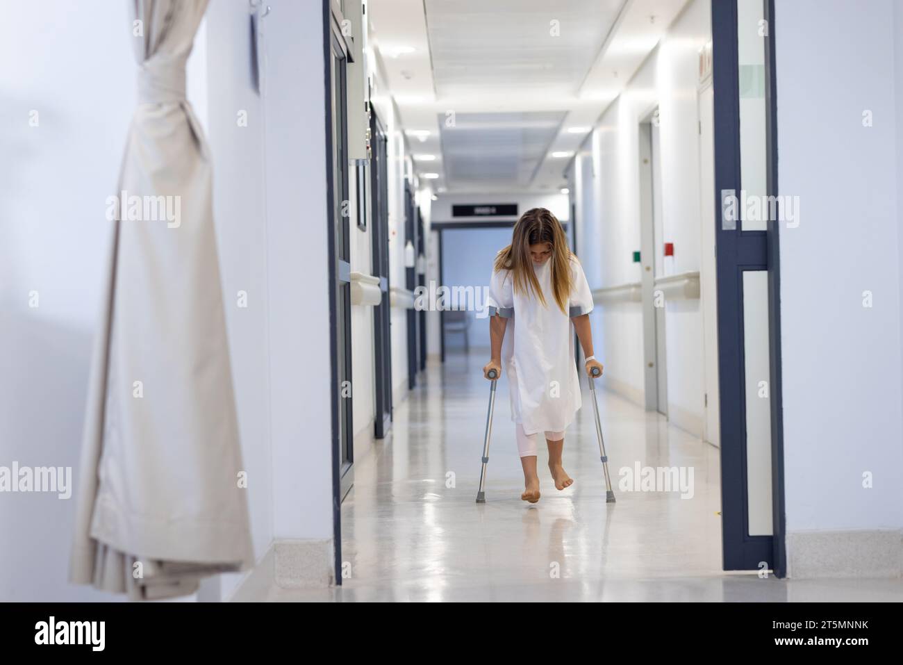 Caucasian girl patient with head down walking with crutches in hospital