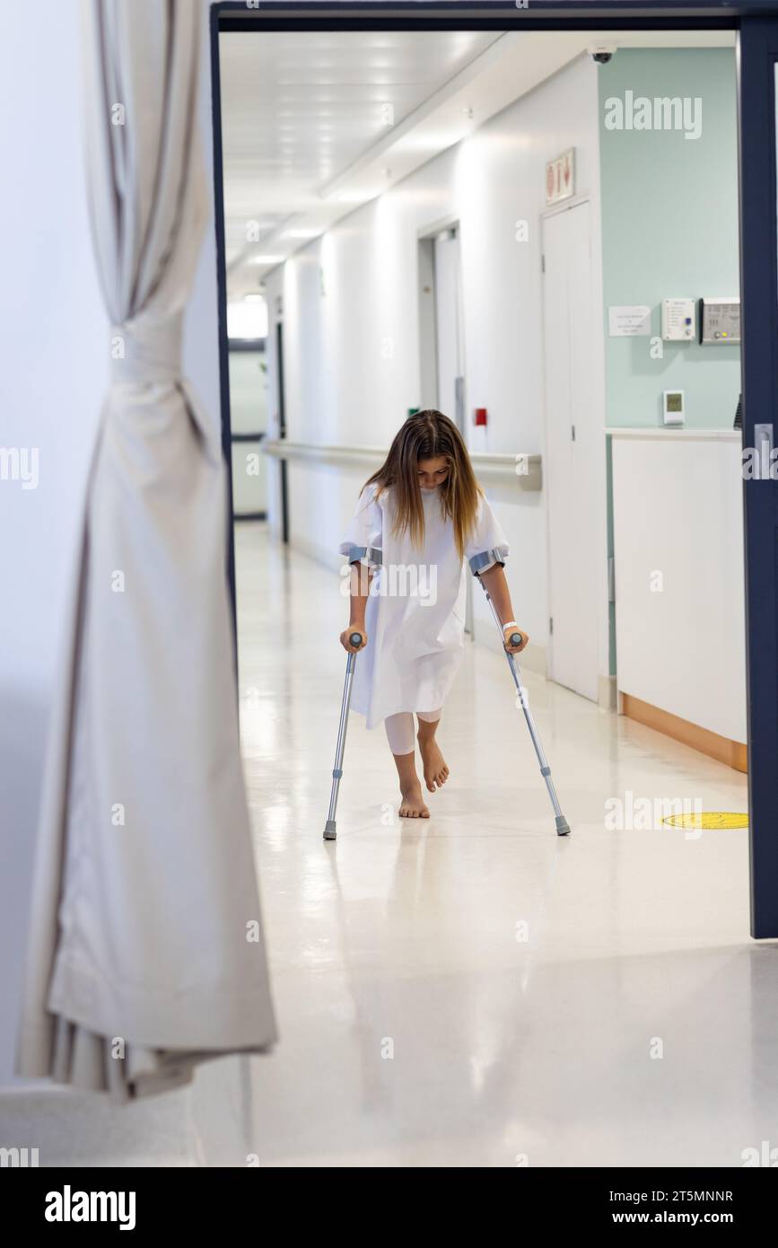 Caucasian girl patient with head down walking with crutches in hospital