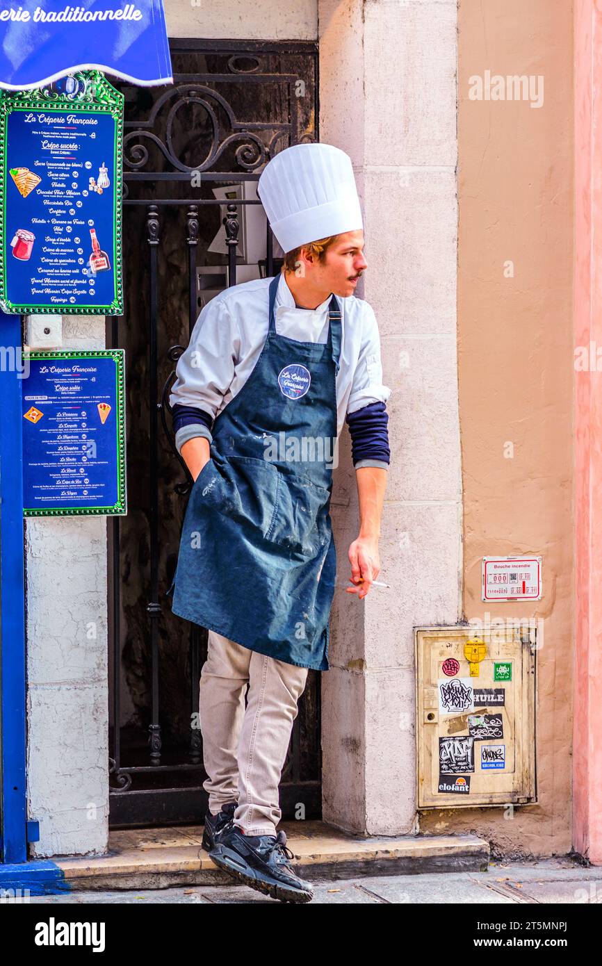 Chef wearing toque and apron taking a smoking break outside La Creperie Francaise, Rue Dauphine, Paris 6, France. Stock Photo
