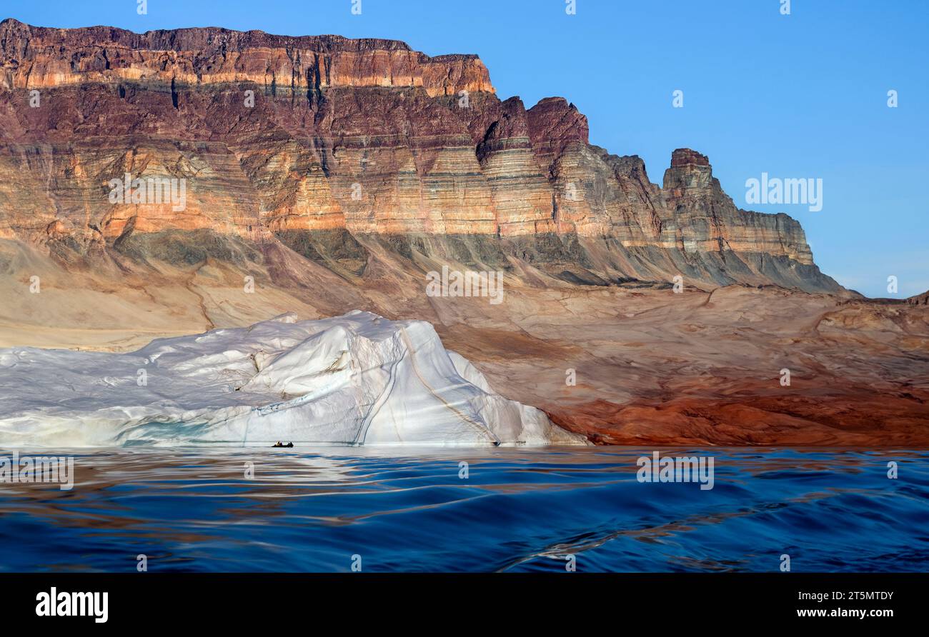 Greenland Rocks Adventure tourists near an iceberg below the sedimentary rocks of Franz ...